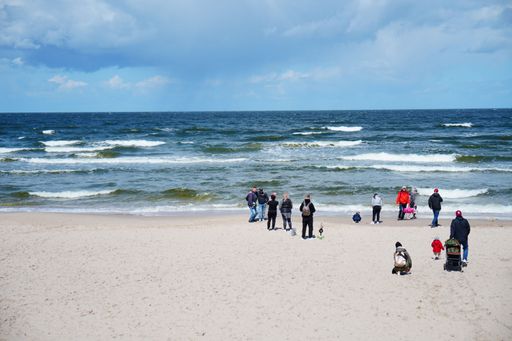 A scenic view of a sandy beach and a group of people standing close by the sea