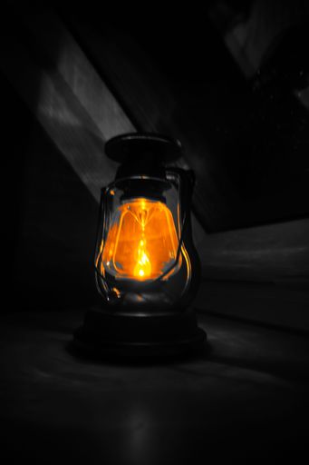 A vertical shot of an old kerosene lamp glowing in the darkness