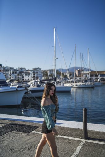 A shallow focus of a young female wearing shorts surrounded by the sea and boats under the sunlight