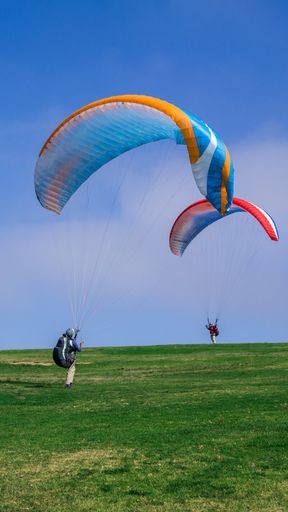 A vertical shot of two persons landing with colorful parachutes on a grassy field. Perfect for a wallpaper or a background