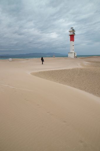 A vertical of a person walking to lighthouse in Badia del Fangar, Delta del Ebre in Catalonia, Spain