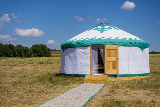 A white yurt (the house of nomadic people, Bashkiria) stands in the steppe with an open door against a blue summer sky
