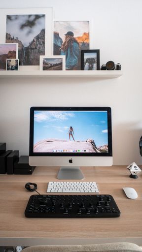 A vertical shot of a minimal desk with an Apple iMac, keyboard, mouse, and photo frames above