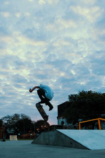 A vertical shot of a Caucasian man doing tricks with a skateboard at sunset
