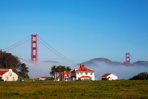 The blue sky over the Golden Gate Bridge captured from the field with houses and palms in summer