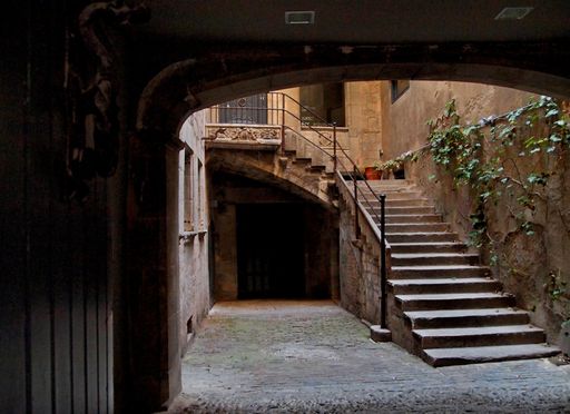 An ancient courtyard with a staircase and plants growing in the walls in Spain, Girona