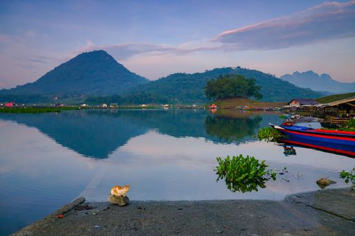 A Landscape with mountains and trees reflecting on lake water under a blue sky