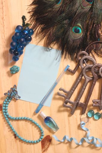 A closeup of notepaper and pen on a wooden table surrounded by peacock feathers and jewelry