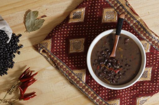 A top view of black bean chili on a wooden table with spices and dried black beans