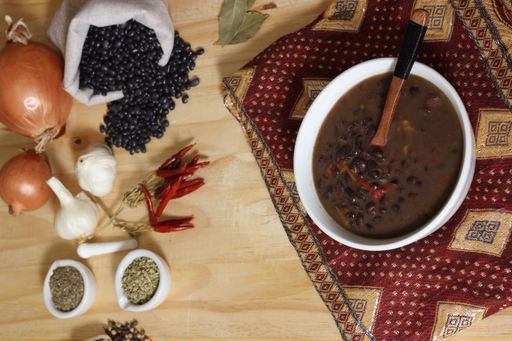 A top view of black bean chili on a wooden table with spices and dried black beans