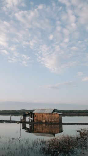 A vertical shot of a wooden hut with its reflection on the lake under the blue sky