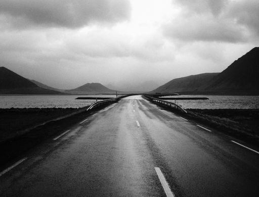 A narrow road bridge with a beautiful sky and a lake shot in black and white