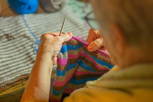 A close up shot of a grandmother knitting a sweater from colorful thread yarns
