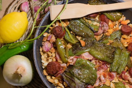 A close up shot of a traditional dish made of sausages, pepper, meat, served with onion and lemon