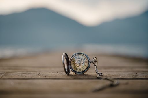 A shallow focus shot of a vintage Pocket Watch on a wooden texture surface with blurred mountains