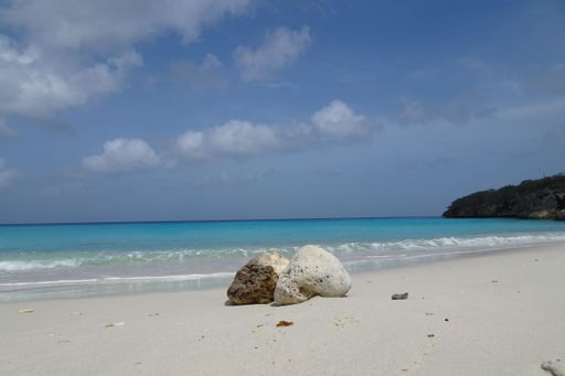 A mesmerizing scene of two huge stones on the sandy beach by the tranquil sea water with a blue sky