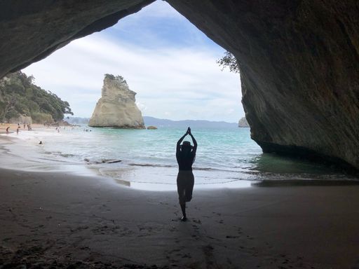 A beautiful view of a female meditating in the Cathedral Cove by the sunny sea water in New Zealand