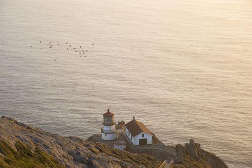 A high angle shot of a lighthouse on the cliff near the sea