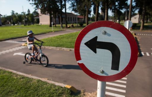 A closeup shot of a traffic sign showing direction with a boy riding a bicycle in the background