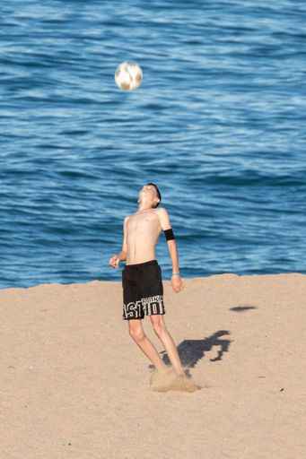A young boy playing with a ball on a Mediterranean beach in summer