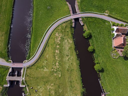 A top view of a curving road running across two small rivers and along grass fields