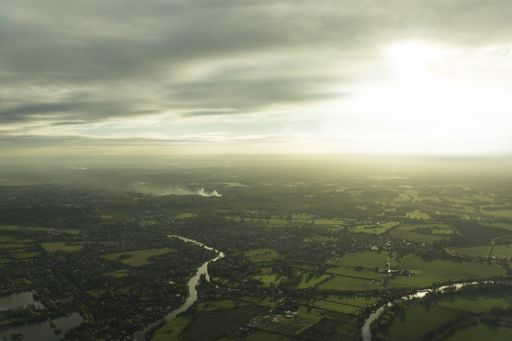 An aerial shot of rivers in the middle of grassy fields with trees under a cloudy sky