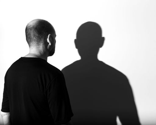 A portrait of a Caucasian man looking at his shadow against a white wall in grayscale