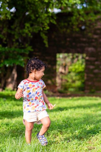 A vertical shot of an Indian small boy with curly hair walking outdoors in the park.