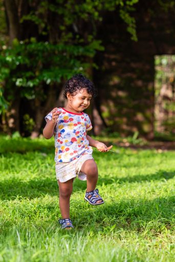 A vertical shot of an Indian small boy with curly hair walking outdoors in the park.