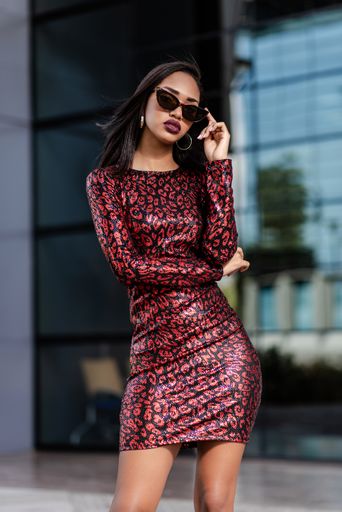 A young African-American woman in a sexy red dress touching her sunglasses near a modern building