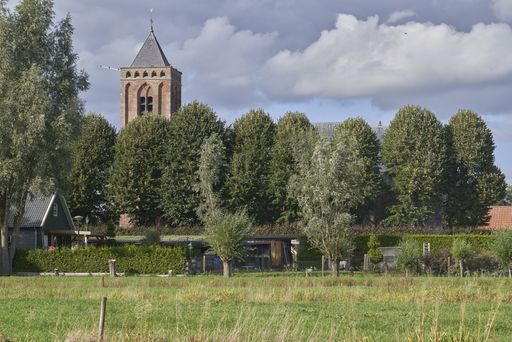 A grassy field with trees and a church tower in the distance under a cloudy sky