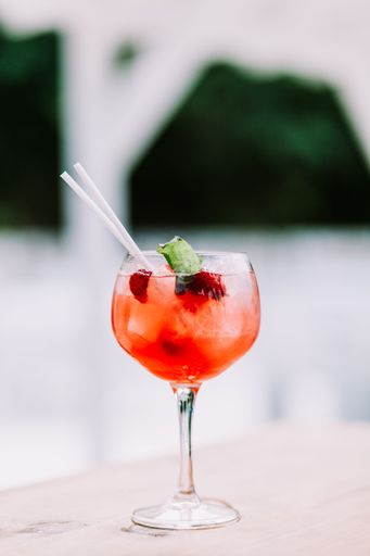 A vertical closeup of a strawberry cocktail with ice and straws on a wooden surface