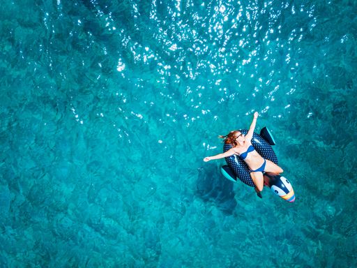 An aerial view of woman wearing beach cloth floating on the water mattress in turquoise sea