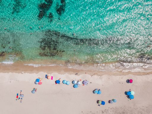 An aerial view of the sea coast with colorful umbrellas on a sunny day in Greece