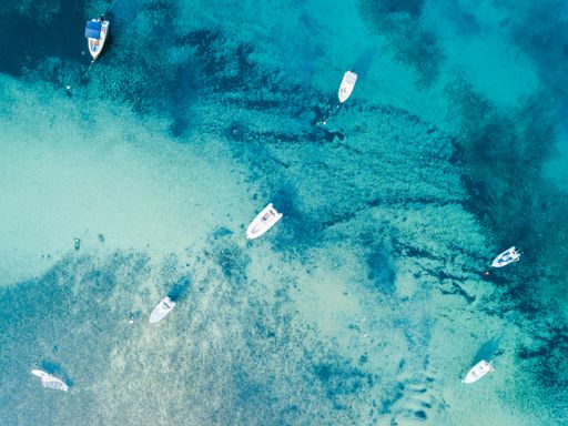 An aerial top-view of white boats in a beautiful marble sea on a sunny day in Greece