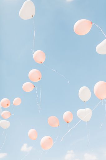 A vertical shot of white and pink balloons in the clear sky