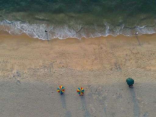 An aerial view of a seaside with people resting under colorful umbrellas