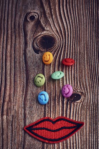 A closeup shot of colorful buttons with smiley faces and a mouth clothes sticker on a wooden table