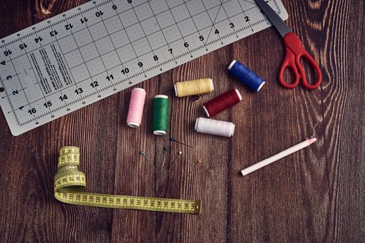 A closeup shot of a tape measure pins colorful threads and other sewing tools on a table