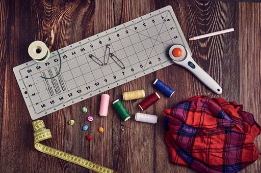 A closeup shot of a tape measure pins colorful threads and other sewing tools on a table