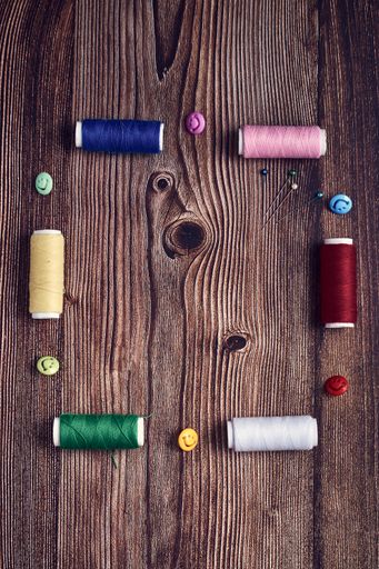 A vertical shot of colorful sewing thread buttons and pins on a wooden table