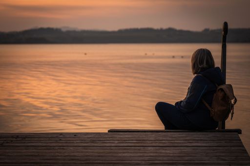 A lonely person sitting on a pier and looking at the beautiful 
pink sunset