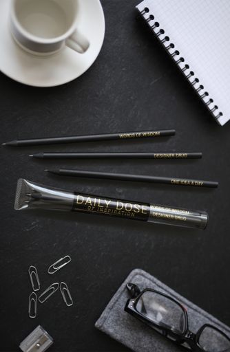 An overhead vertical shot of pencils near a notebook and a coffee mug on a black surface
