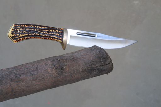 A closeup of a hunting knife on wood under the lights with a blurry background