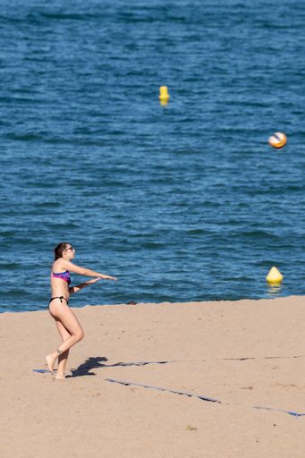 A vertical shot of a young woman in bikini playing beach volleyball on a sunny summer day