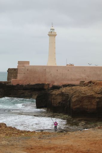 The vertical view of a man fishing by the old lighthouse on a rainy day