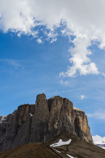 A vertical shot of the Dolomite Mountains with thick clouds above during daylight