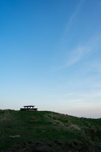 A vertical landscape of a hill with a wooden bench with blue sky above in Italy, Paluzza, Friuli-Venezia Giulia