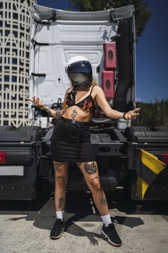 A vertical shot of a female with tattoos wearing a helmet and posing in the back of a truck