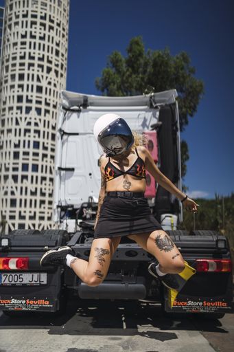 A vertical shot of a female with tattoos wearing a helmet and posing in the back of a truck